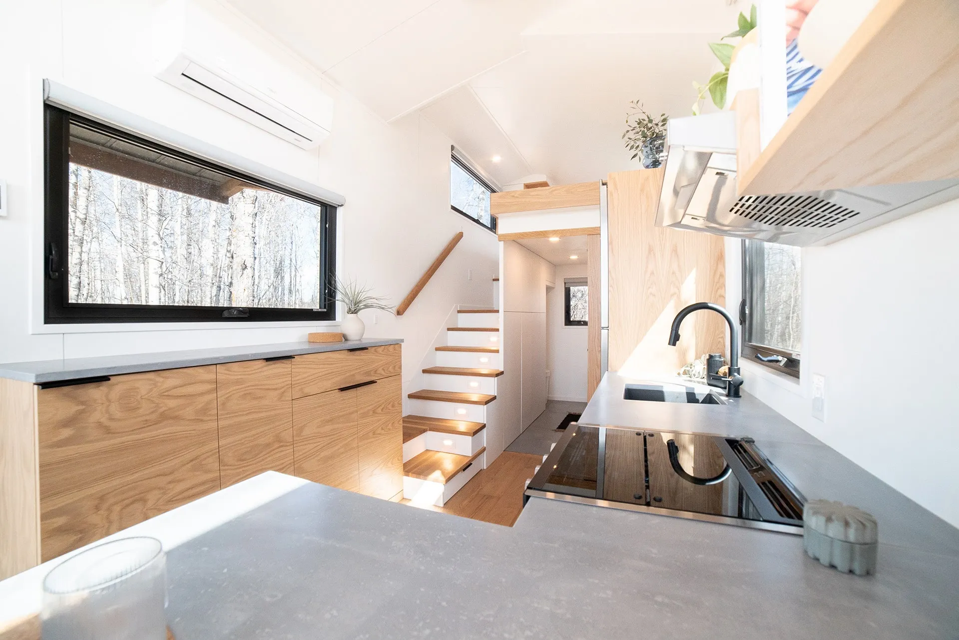 Angled shot of main floor interior of modern kitchen breakfast island and floating storage cabinet, stairs with storage underneath leading up to bedroom